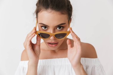 Bir baştan çıkarıcı genç casual esmer kadın güneş gözlüğü beyaz arka plan üzerinde izole kamera bakarak portresi