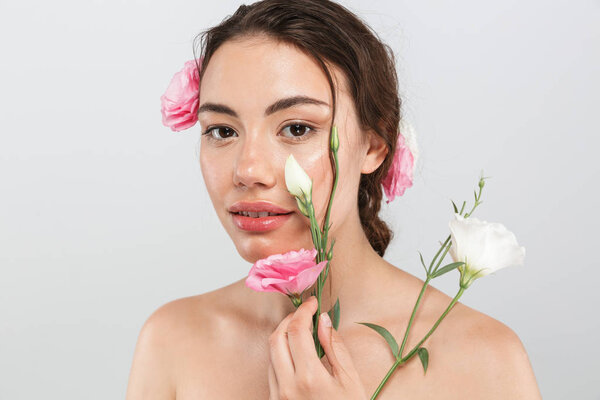 Beauty portrait of a sensual young topless woman with make-up posing with eustoma flowers at her face isolated over gray background