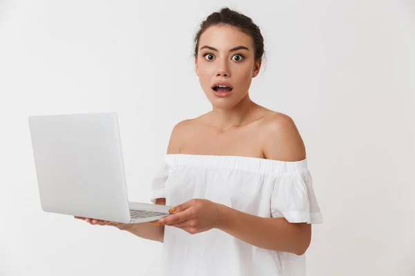 一个震惊的年轻的休闲黑发妇女的肖像手持笔记本电脑隔离在白色背景 — 图库照片