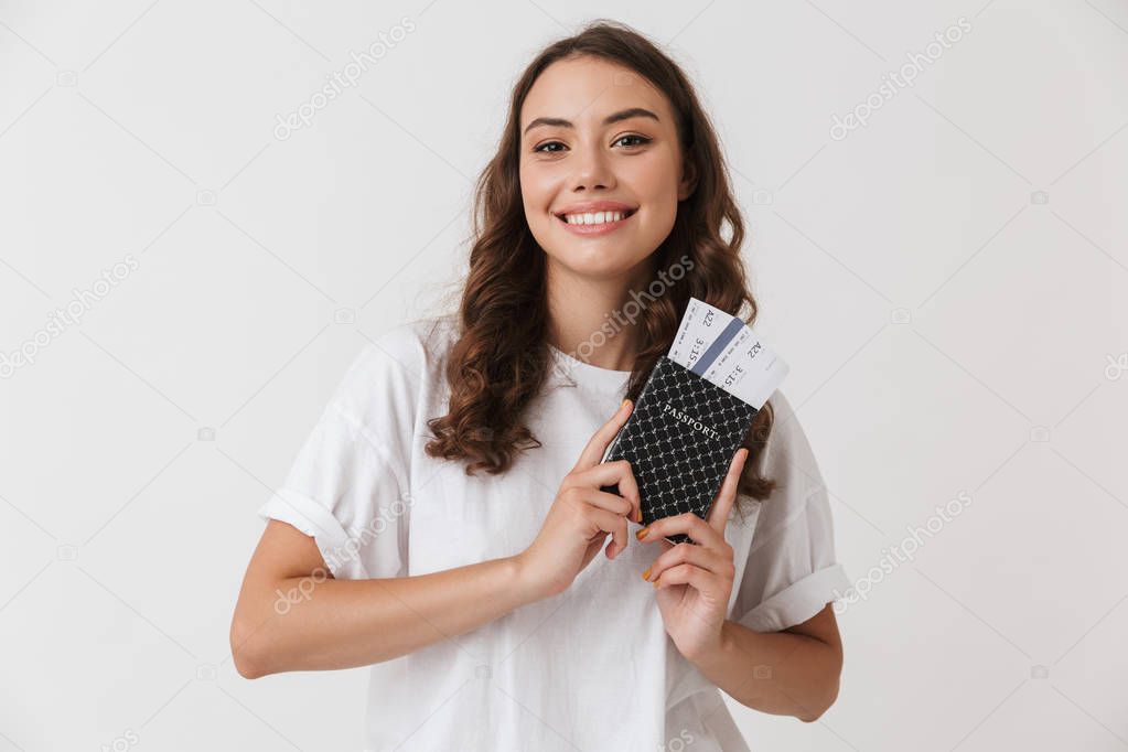 Portrait of a smiling young casual brunette woman holding passport with fying tickets isolated over white background