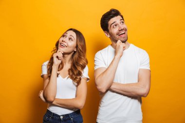 Neşeli genç insanlar erkek ve kadın gülüyor ve seyir bir kenara izole sarı arka plan üzerinde iken çene dokunmadan temel giyim görüntü
