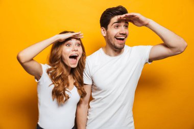 Image of astonished man and woman 20s in basic clothing screaming in surprise or delight and looking aside with hands at foreheads isolated over yellow background clipart