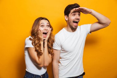 Image of delighted man and woman 20s in basic clothing screaming in surprise and looking aside with hand at forehead isolated over yellow background clipart