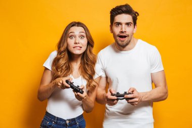 Heyecanlı genç adam ve birlikte oynama ve video oyunları üzerinde sarı arka plan izole joystick kullanarak yarışan kadın görüntüsü