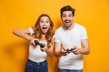 Fotoğraf çift erkek ve kadın birlikte izole sarı arka plan üzerinde joystick kullanarak video oyunları oynama