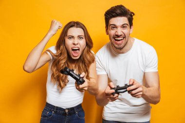 Kendinden geçmiş genç erkek ve kadın birlikte izole sarı arka plan üzerinde joystick ile video oyunları oynarken görüntü