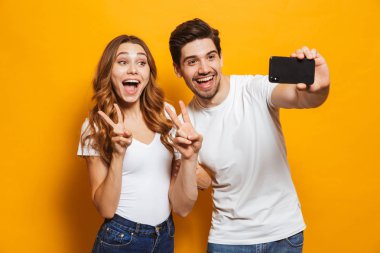 Mutlu bir adam ve kadın selfie smartphone barış sarı arka plan üzerinde izole işareti gösterilen süre fotoğrafta portre