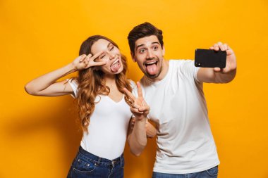 Heyecanlı çift erkek ve kadın selfie smartphone barış sarı arka plan üzerinde izole işareti gösterilen süre fotoğrafta portre