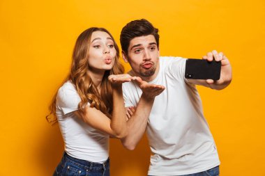 Mutlu bir adam ve selfie fotoğrafta smartphone ve sarı arka plan üzerinde izole kamera hava öpücük üfleme kadın portre