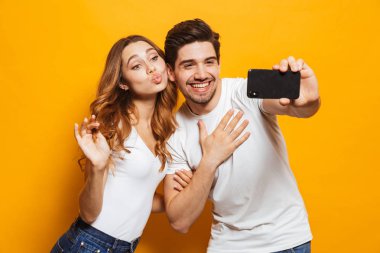 Görüntü güzel içerik erkek ve kadın gülümseyerek ve sarı arka plan üzerinde izole Smartphone cep telefonu ile selfie fotoğraf çekme