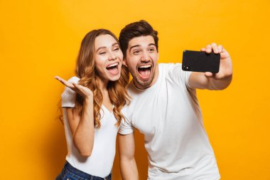 Mutlu genç çift sarı arka plan üzerinde izole cep telefonunuzla selfie alarak