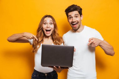 Memnun olumlu erkek ve holding ve izole sarı arka plan üzerinde siyah laptop parmakları işaret kadın portresi