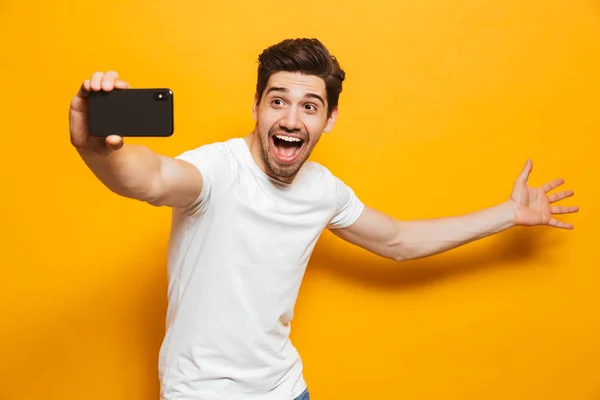 黄色の背景に分離された携帯電話と Sefie を取って幸せな若い男の肖像 — ストック写真