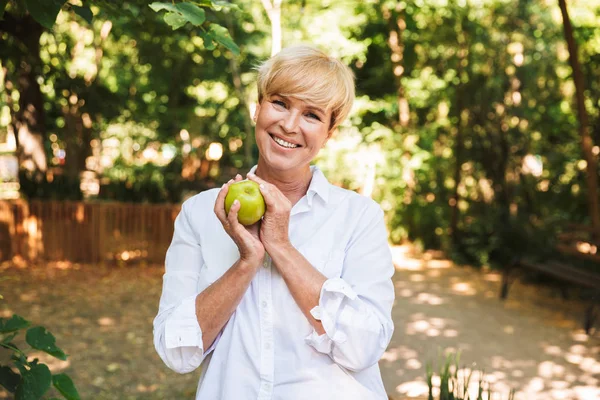 Счастливая Зрелая Женщина Держит Зеленое Яблоко Стоя Парке — стоковое фото