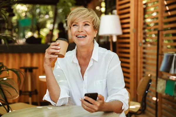 Смех Зрелой Женщины Держащей Мобильный Телефон Сидя Кафе Попивая Кофе — стоковое фото