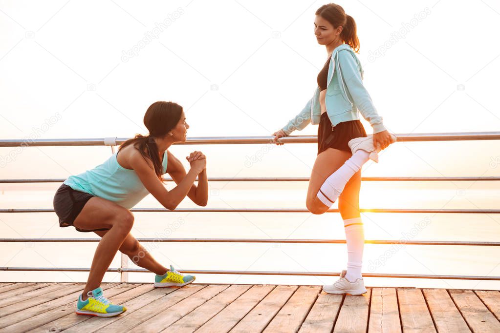 Photo of strong young two sports women friends outdoors on the beach make sport exercises.