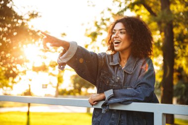 Neşeli Afrikalı kız parkta iyi vakit, parmak işaret denim ceket