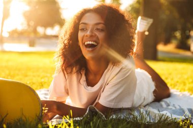 Mutlu genç Afrikalı kadın görüntüsünü çim açık havada kaykay parkı üzerinde yatıyor.
