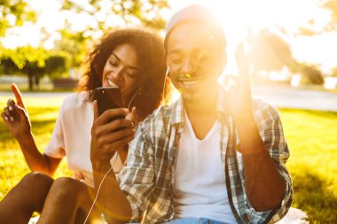 Genç, neşeli bir Afrika çift kulaklık parkta birlikte müzik dinlemek içinde portresi