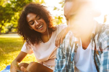 Genç, neşeli bir Afrika çift kulaklık parkta birlikte müzik dinlemek içinde portresi