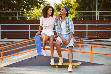 Çekici bir genç Afrikalı çift ile birlikte paten parkta oturan kaykaylar portresi