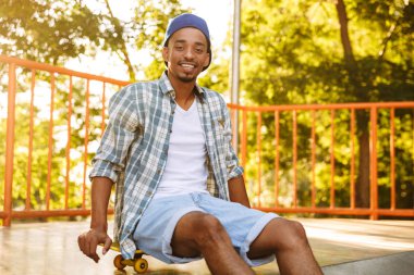 Afrika delikanlı bir rampa üzerinde paten parkta oturan kaykay ile gülümseyen