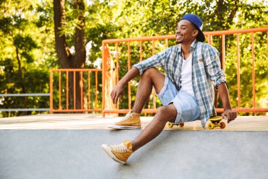 Kaykay bir rampa üzerinde paten parkta oturan genç Afrika adamla neşeli