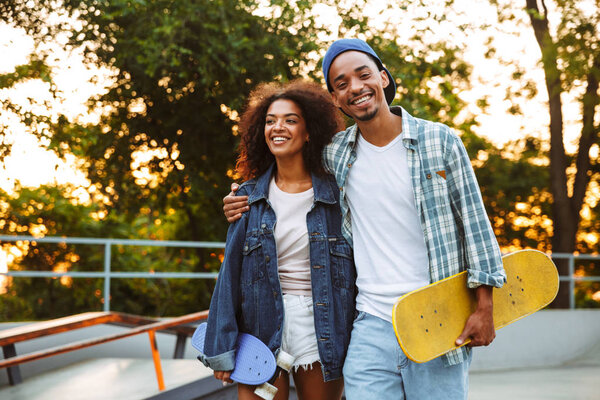 Portrait of a happy young african couple with skateboards standing together at the skate park
