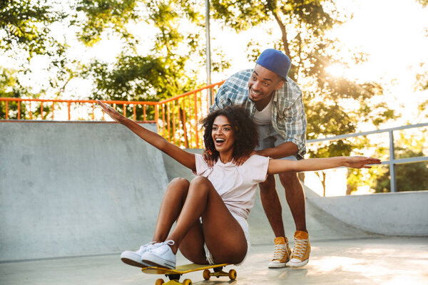 Portrait of a happy young african couple with skateboards having fun together at the skate park