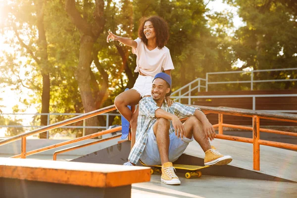 スケート ボード親指を示すスケート公園で一緒に座っていると陽気なアフリカのカップルの肖像画 — ストック写真