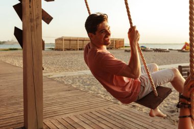 Arkadaşlar açık havada salıncakta sürme sahilde resmini.