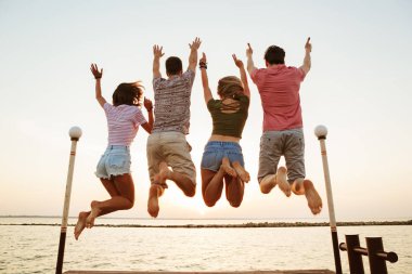 Grup dört arkadaşıyla kumsalda açık havada atlama çiftler sevgi dolu görünümü görüntü geri.