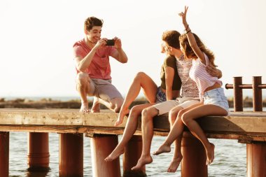 Açık havada sahilde oturan arkadaş grubu resim çekmek için fotoğraf.