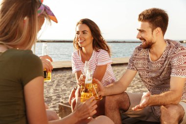 Neşeli arkadaş grubu yaz giyim sahilde bira şişeleri ile toasting içinde giyinmiş