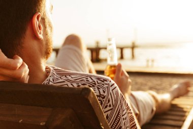 Yakışıklı adam resmi var bir dinlenme açık havada sahilde bira içmek.