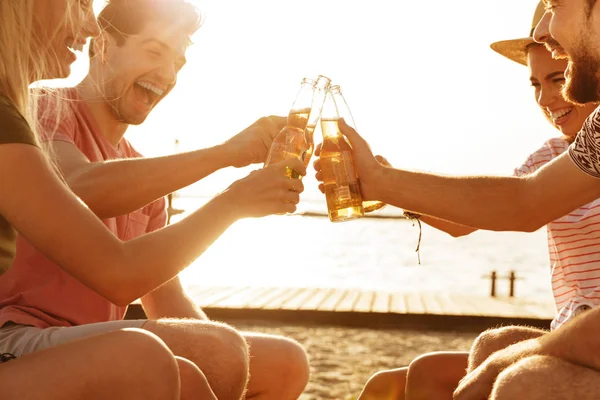 一群兴奋的朋友穿着夏天的衣服在海滩上用啤酒瓶敬酒 — 图库照片