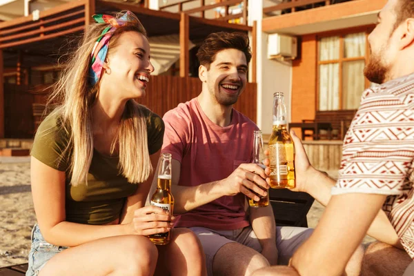 一群笑着的朋友穿着夏天的衣服在海滩上喝啤酒 — 图库照片