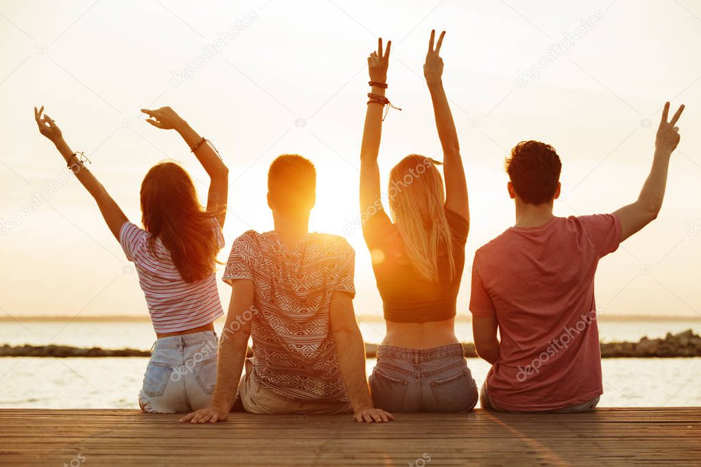 Back view photo of group of four friends loving couples walking outdoors on the beach showing peace gesture.