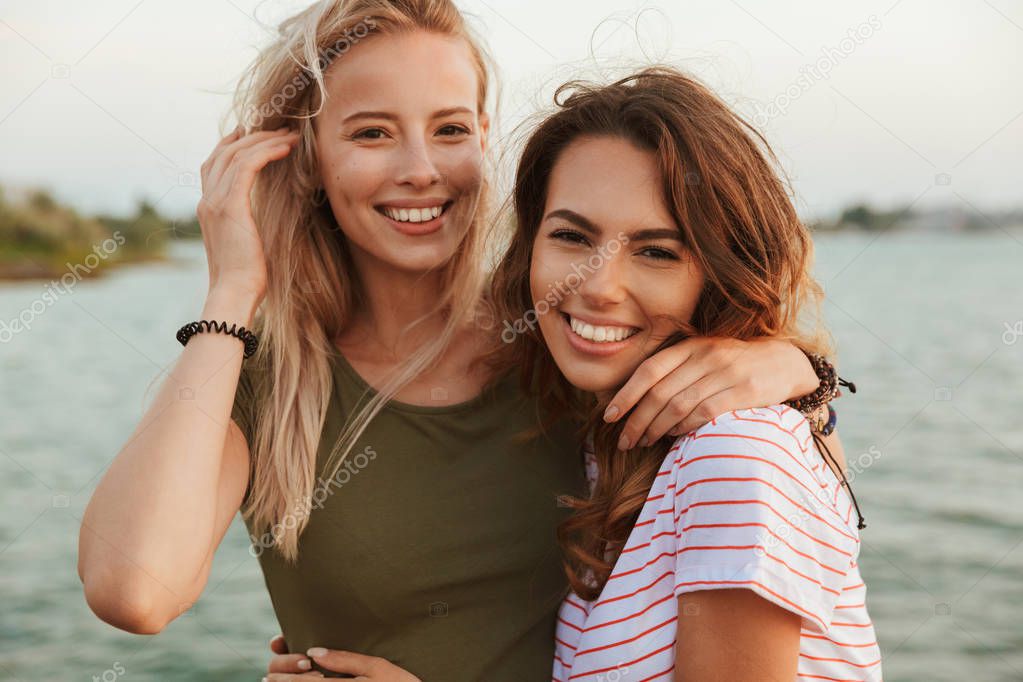 Image of two happy women friends hugging outdoors on the beach.