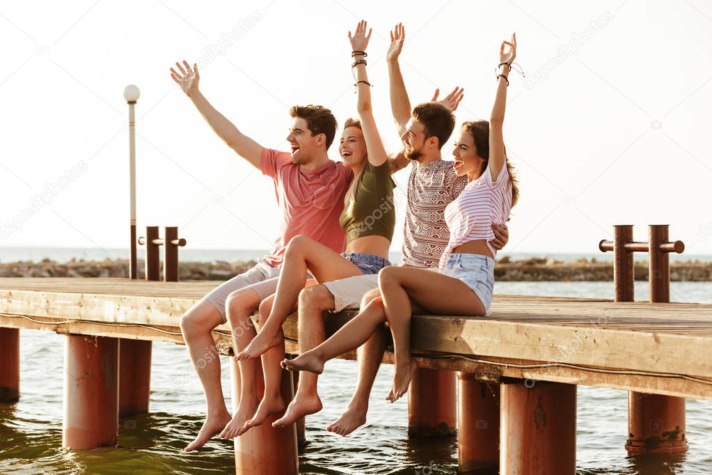 Picture of group of four friends loving couples sitting outdoors on the beach.