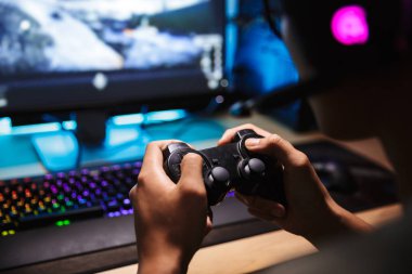 Kulaklık mikrofon ile giyen ve joystick kullanarak karanlık odada bilgisayarda video oyunları oynarken Asya oyun çocuk closeup fotoğraf