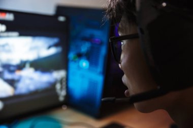 Fotoğraf closeup bilgisayarda kulaklık mikrofon ile giyiyor ve arkadan aydınlatmalı renkli klavye kullanarak karanlık odada video oyunları oynarken Asya oyun çocuk heyecanlı