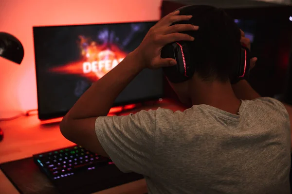 ヘッドフォンを身に着けている暗い部屋でコンピューターでビデオ ゲームをプレイ 代のゲーマー少年裏から肖像画 — ストック写真