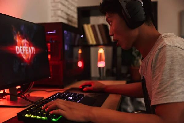 ビデオ ゲームをプレイしながら失うアジアの 代のゲーマー少年の肖像ヘッドフォンを身に着けていると カラフルなキーボードのバックライトを使用して暗い部屋でコンピューターの — ストック写真