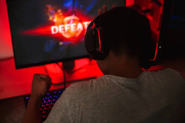 ヘッドフォンを身に着けている暗い部屋でコンピューターのビデオゲームの若いゲーマー男裏から肖像画 — ストック写真