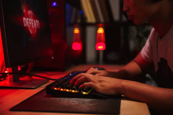 亚洲青少年游戏玩家男孩丢失视频游戏的形象在黑暗的房间里玩电脑戴着耳机 使用背光彩色键盘 — 图库照片