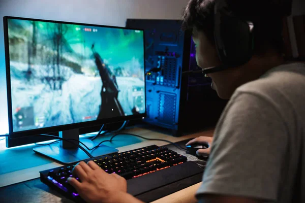 マイク付きヘッドフォンを着用し バックライト付きカラフルなキーボードを使用して暗い部屋でコンピューターのゲームをオンラインでビデオを再生アジアの幸せなゲーマー少年の肖像画 — ストック写真