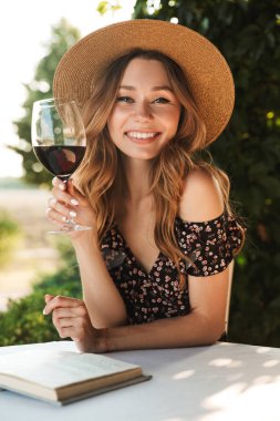 Şarap içme cam elinde kitapla café outdors parkta oturan sevimli genç ve güzel kadın görüntüsünü.