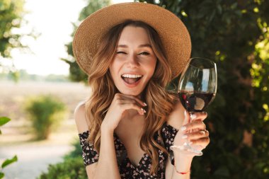 Café outdors şarap içme cam holding Park içinde oturan genç ve güzel kadın görüntüsünü.