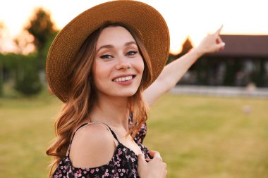 Hasır şapka gülümseyen ve açık yeşil alan kırsal kesimde yürürken neşeli güzel kadın fotoğrafı